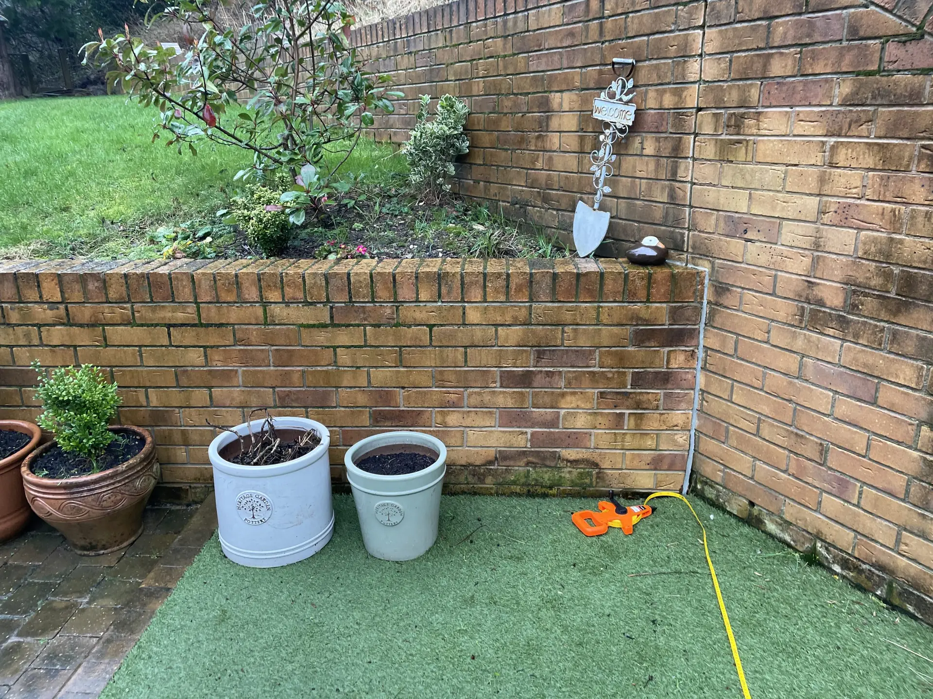 Tape measure laid across artificial lawn beside a brick wall corner during the site survey